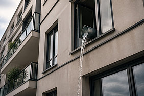 Modernes Wohnhaus mit offenem Fenster, aus dem Wasser aus einem Eimer nach unten geschüttet wird.